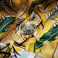 Een gouden Citizen horloge op een geel bloemenhemd.
