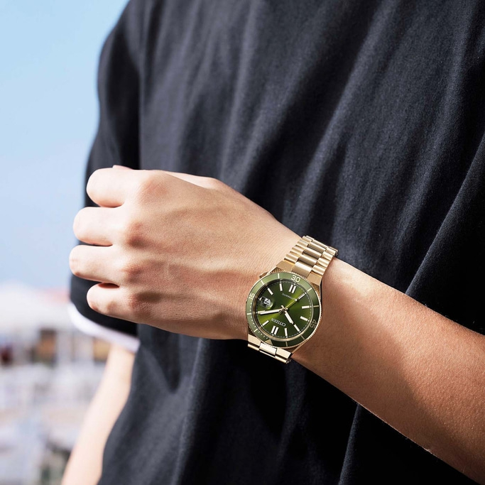 Man draagt een gouden Citizen horloge met groene wijzerplaat.