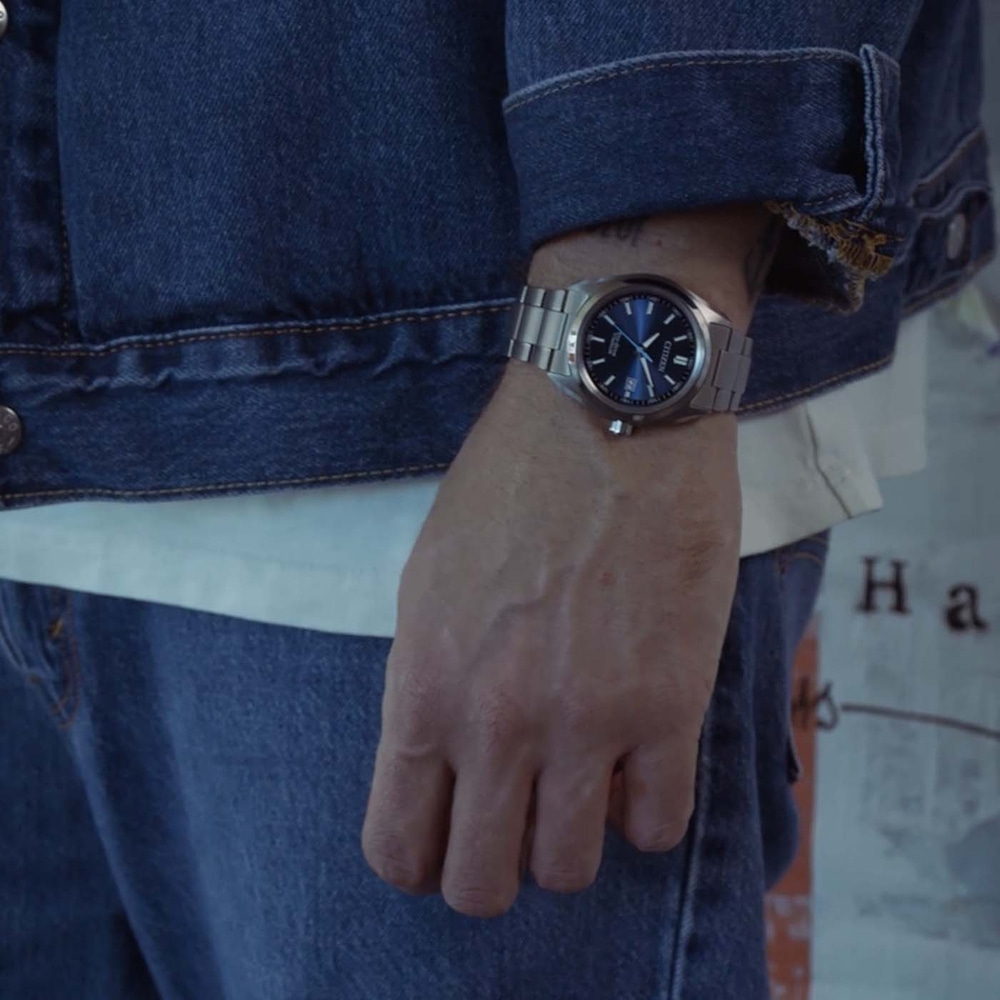 Man draagt een blauw spijkerjack, wit T-shirt en spijkerbroek met horloge