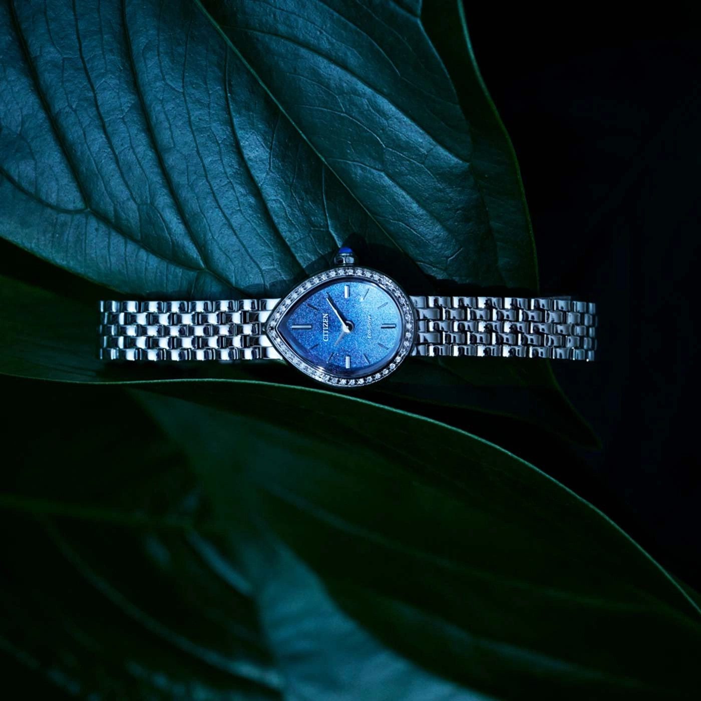 Een druppelvormig horloge met diamantjes op een blad