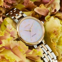Citizen horloge met gouden en zilveren band, omringd door gele bloemen.