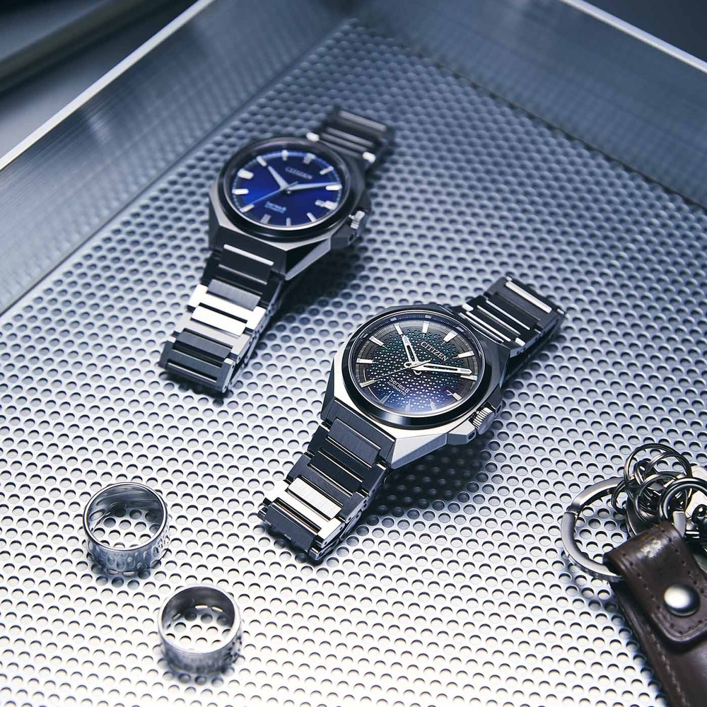 Twee horloges, ringen en een sleutelhanger op een getextureerd oppervlak.