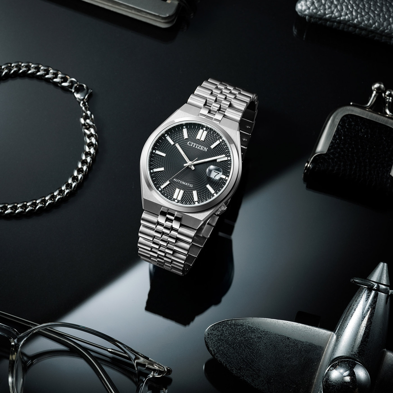 Citizen horloge met armband, bril en accessoires op zwart oppervlak.