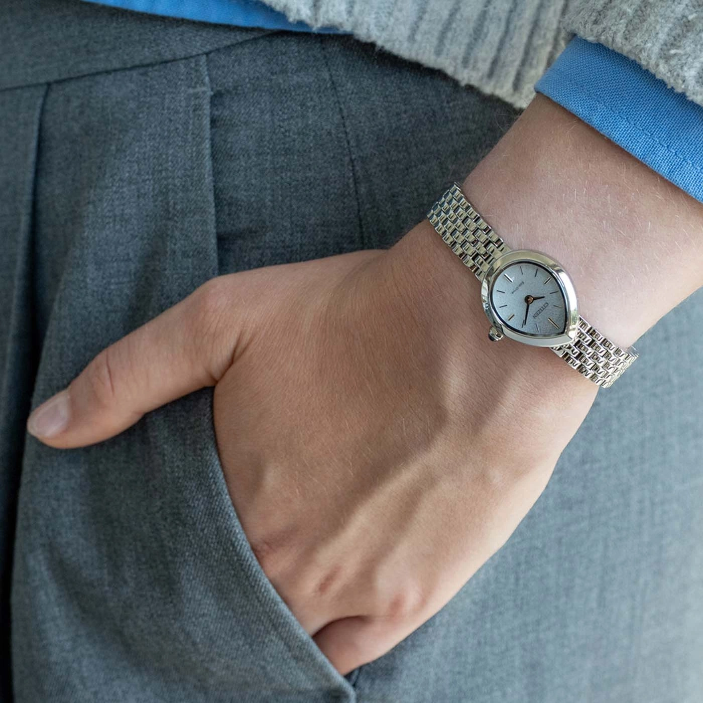 Persoon draagt een zilveren horloge om de linkerpols, hand in de zak.