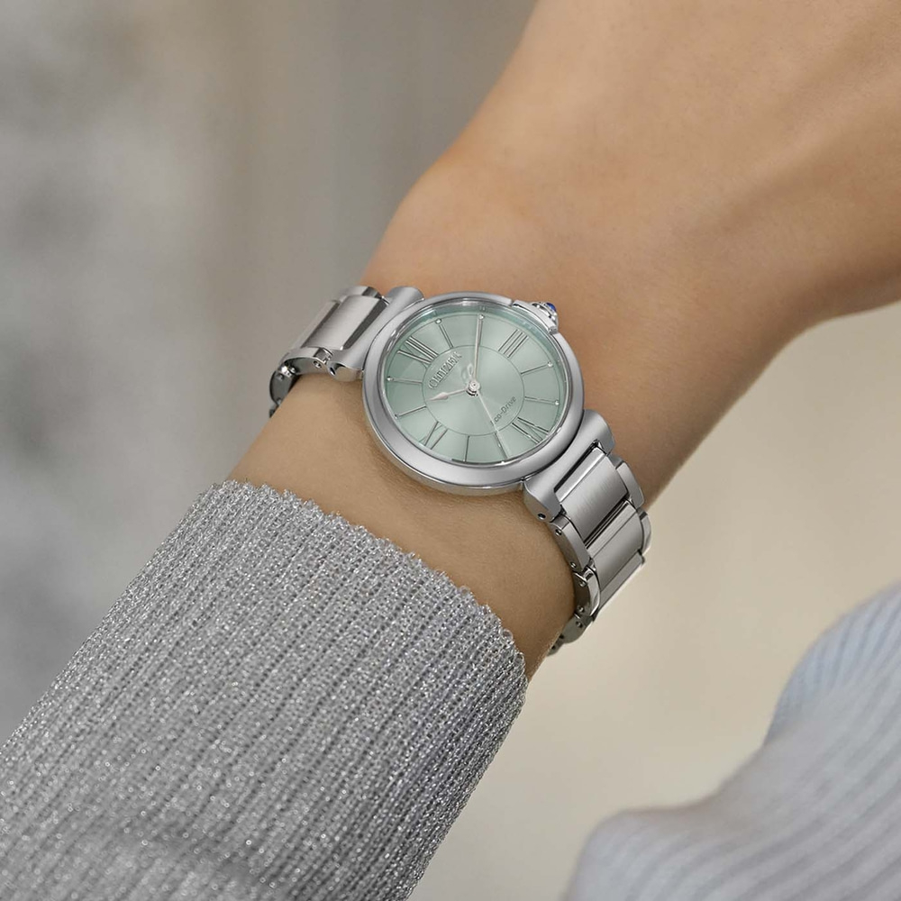 De pols van een vrouw met een zilveren horloge met een lichtgroene wijzerplaat.