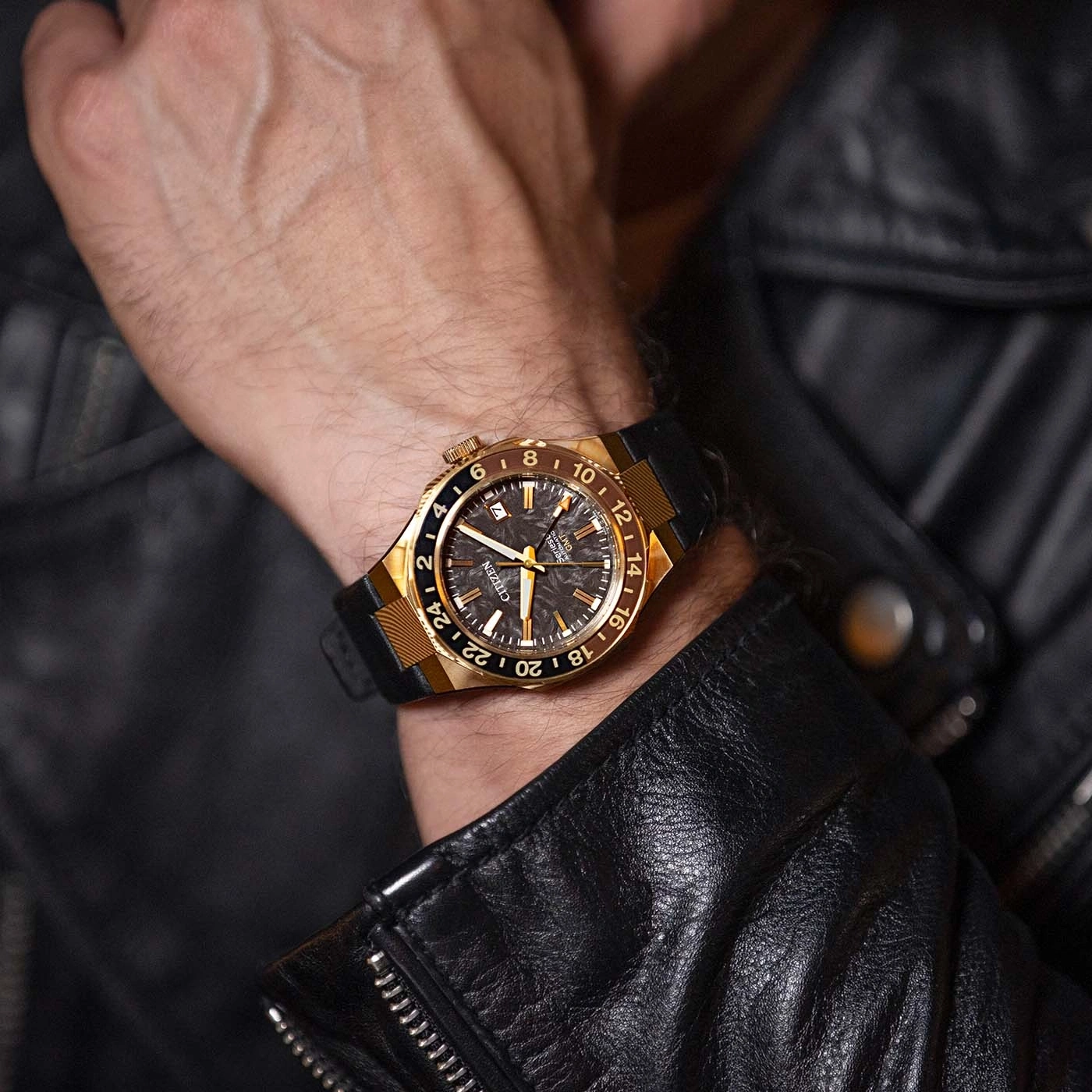 Een man draagt een goud-zwart Citizen horloge om zijn pols, gekleed in een zwarte leren jas.