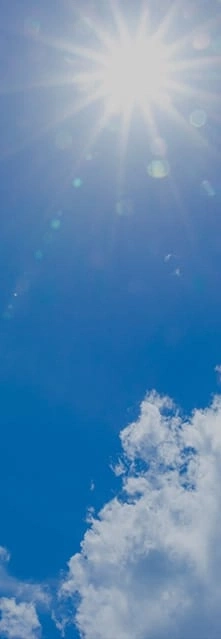 Felle zon in een blauwe lucht met wat pluizige witte wolken.