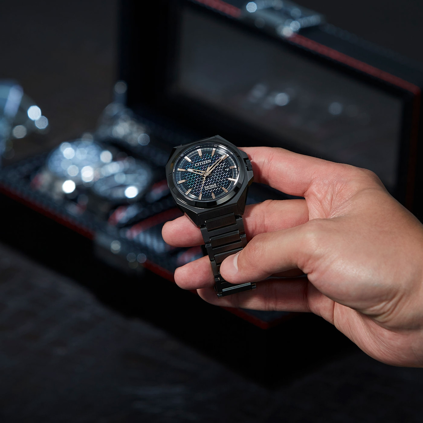 Een persoon die een zwart Citizen-horloge vasthoudt met een donkere achtergrond.