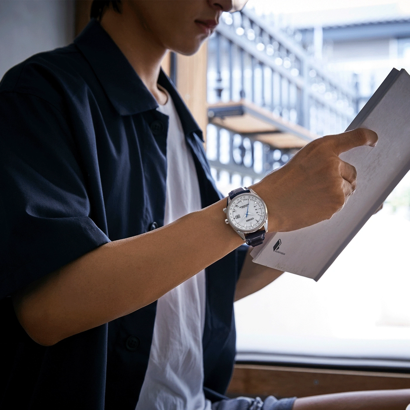 Man met horloge, leest papier, met blauwe jas en wit overhemd.
