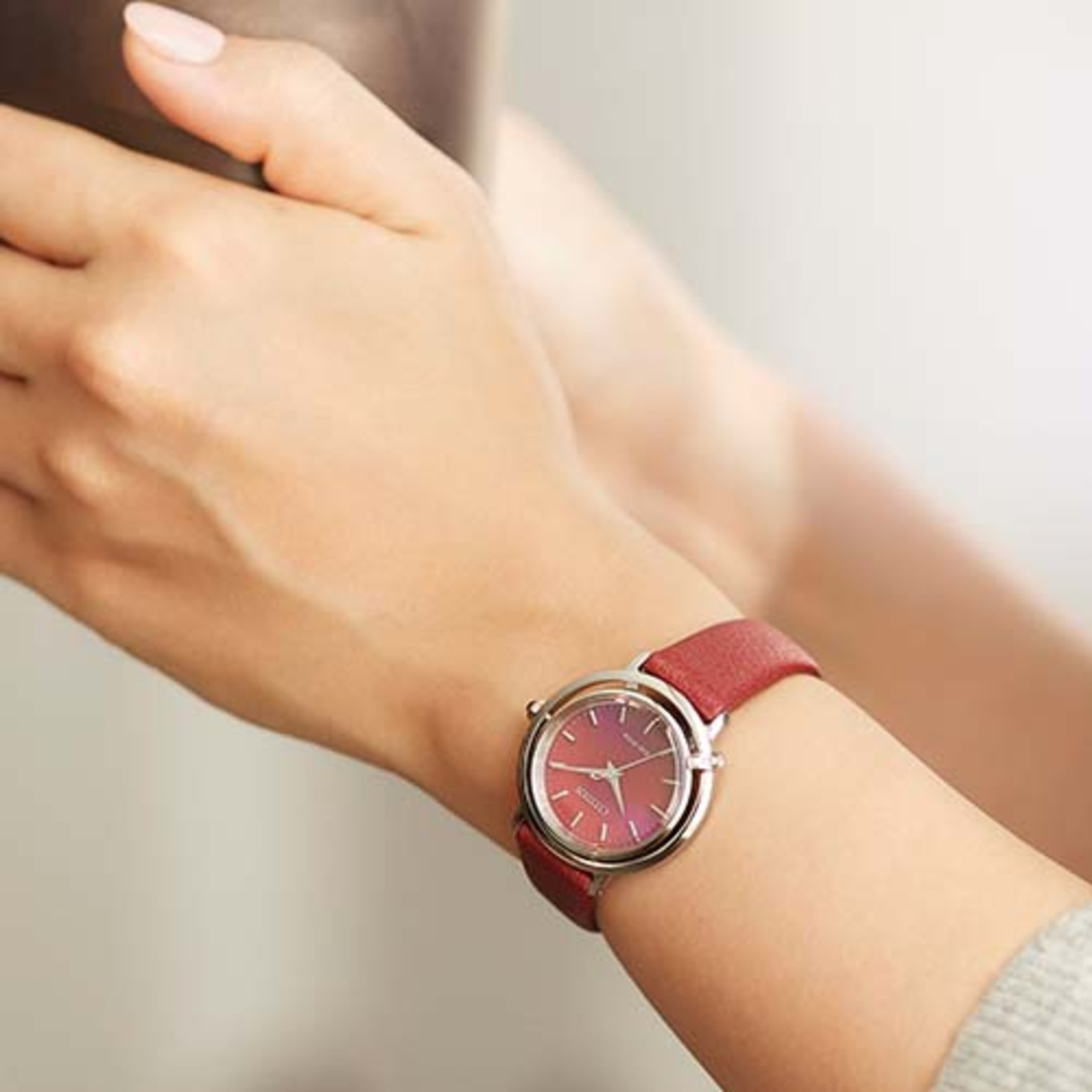 Een pols van een vrouw met een rood horloge. Het horloge heeft een rode band en een zilveren kast.