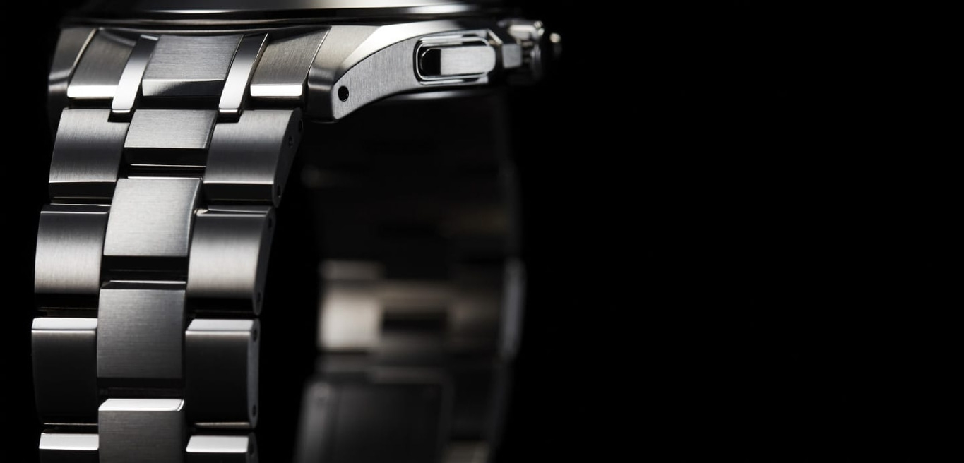 Close-up van een zilveren horloge met een zwarte achtergrond, met de band van het horloge.