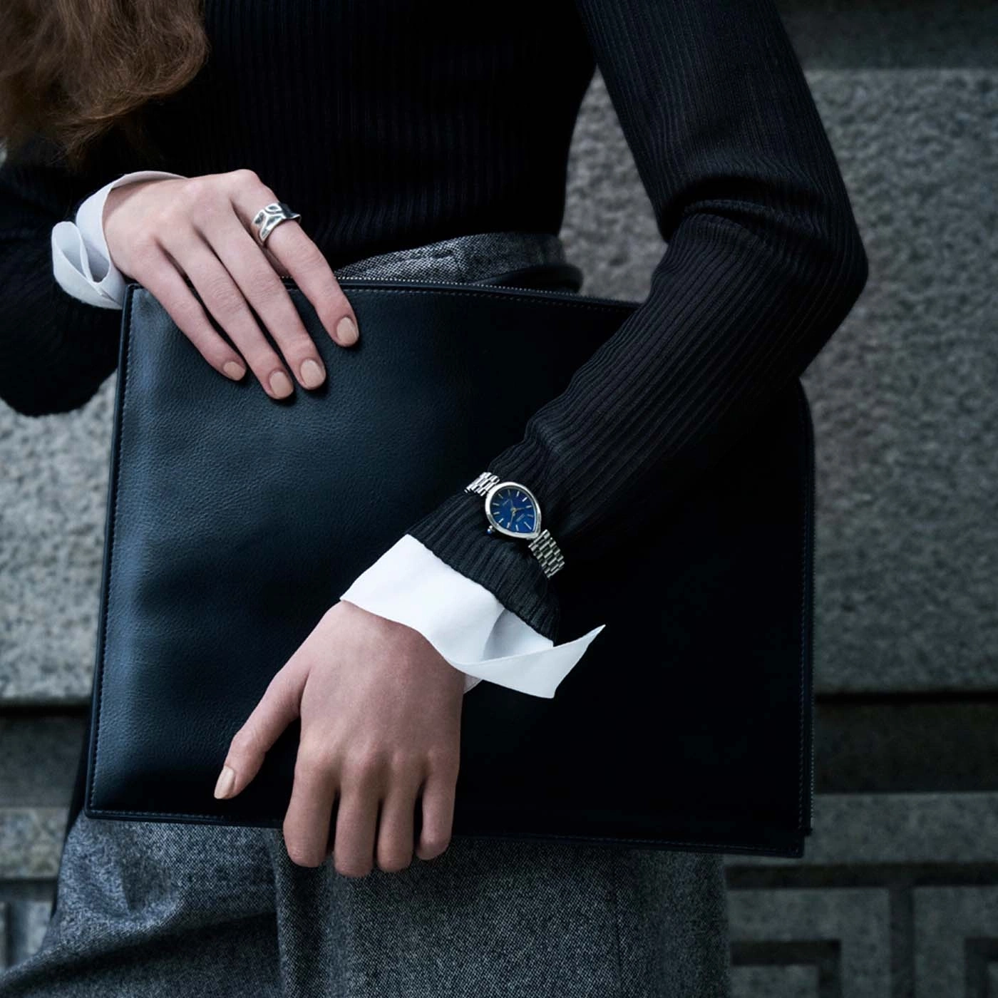 Vrouw houdt zwarte aktetas vast, draagt horloge en ring.