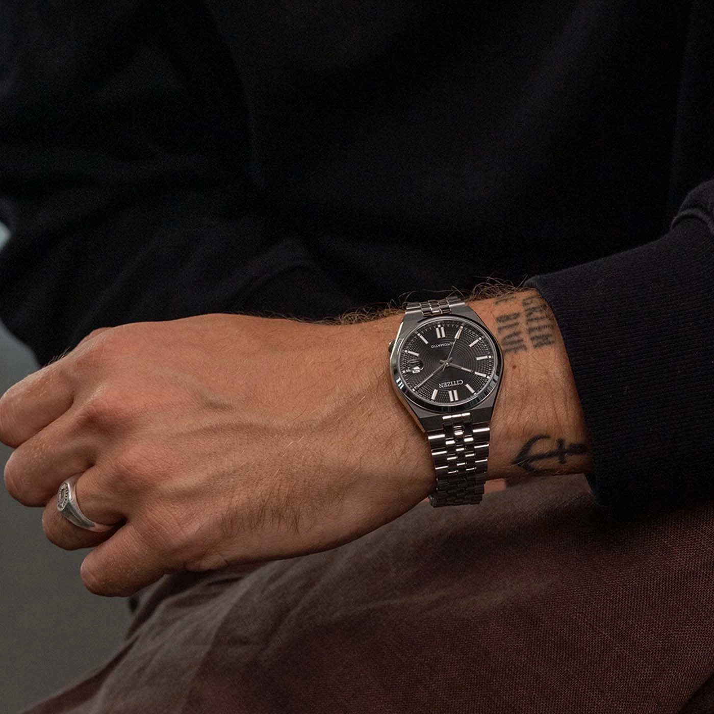 Man draagt een zwart Citizen automatisch horloge met zilveren band en ring.
