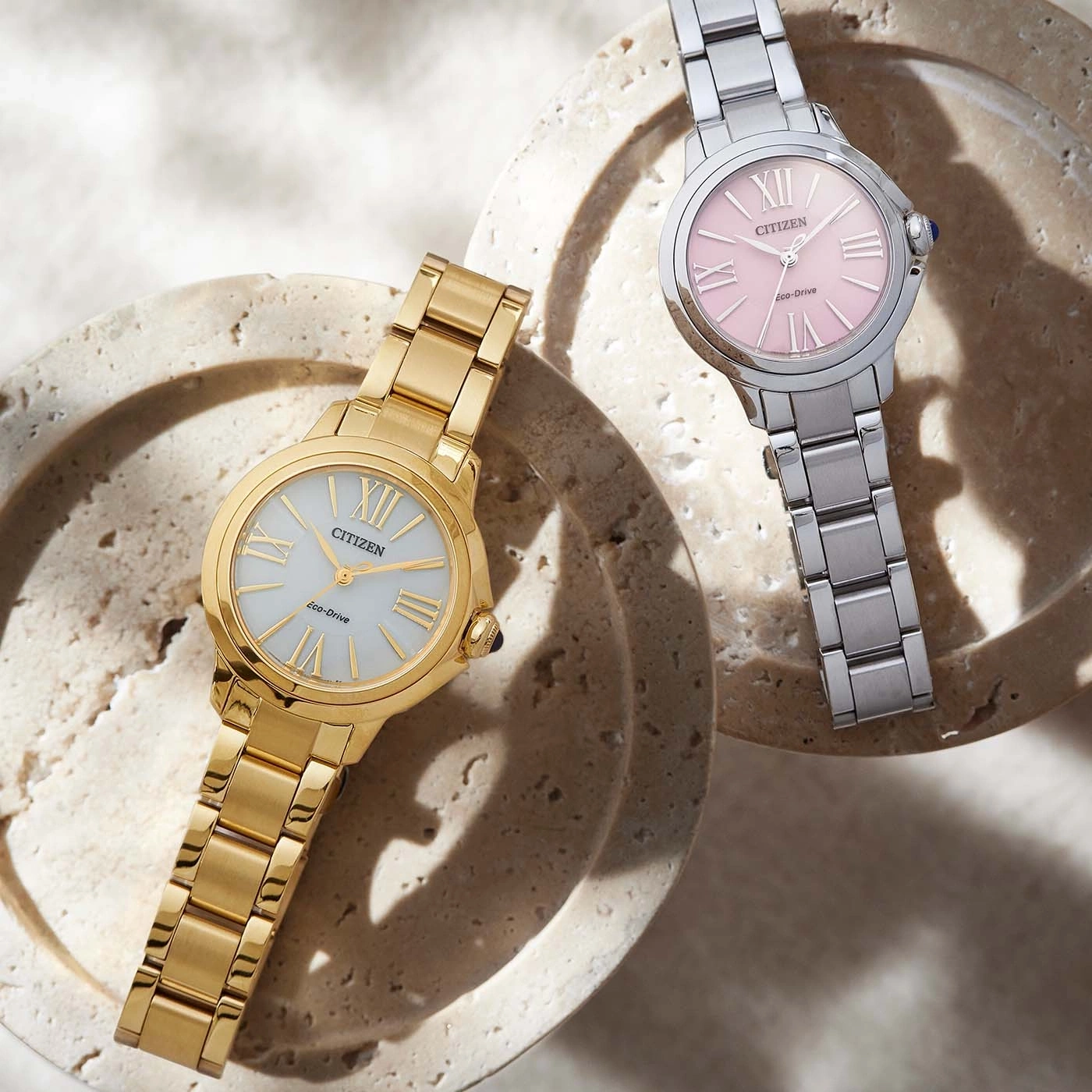 Twee Citizen horloges, goud en zilver, op een getextureerd oppervlak.