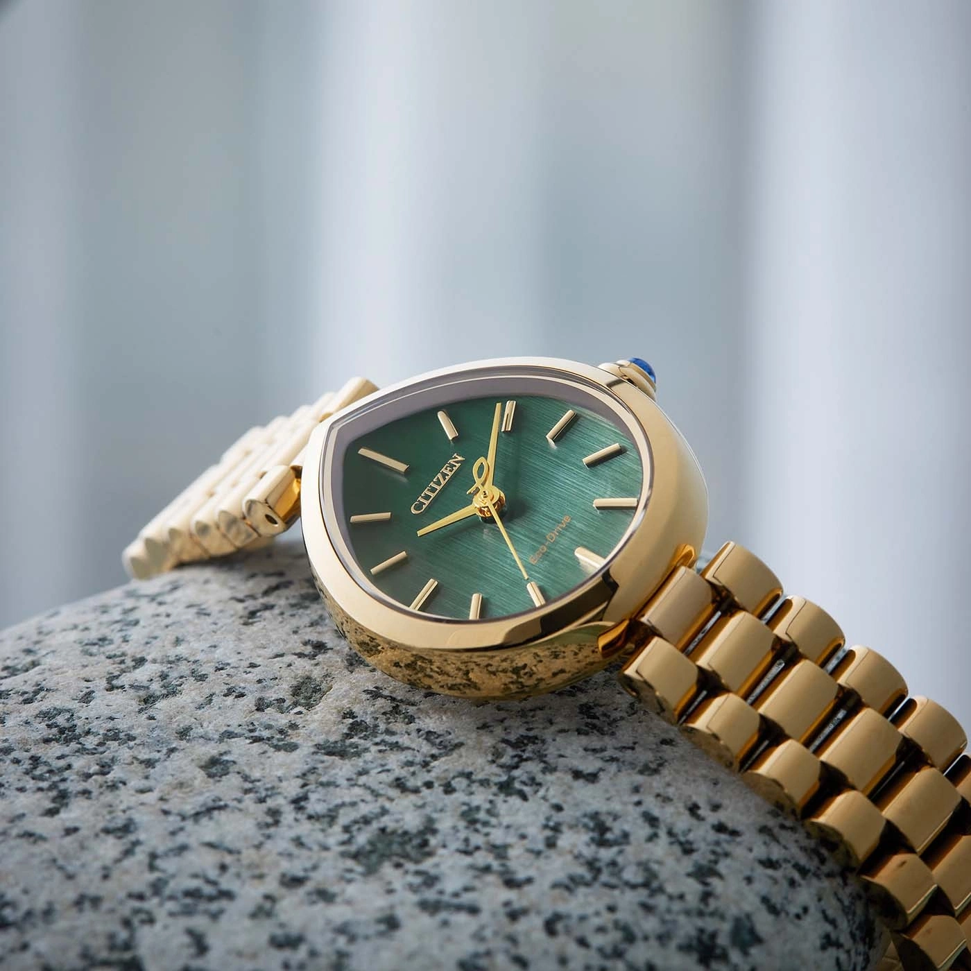 Een gouden Citizen Eco-Drive horloge met groene wijzerplaat rust op een steen.