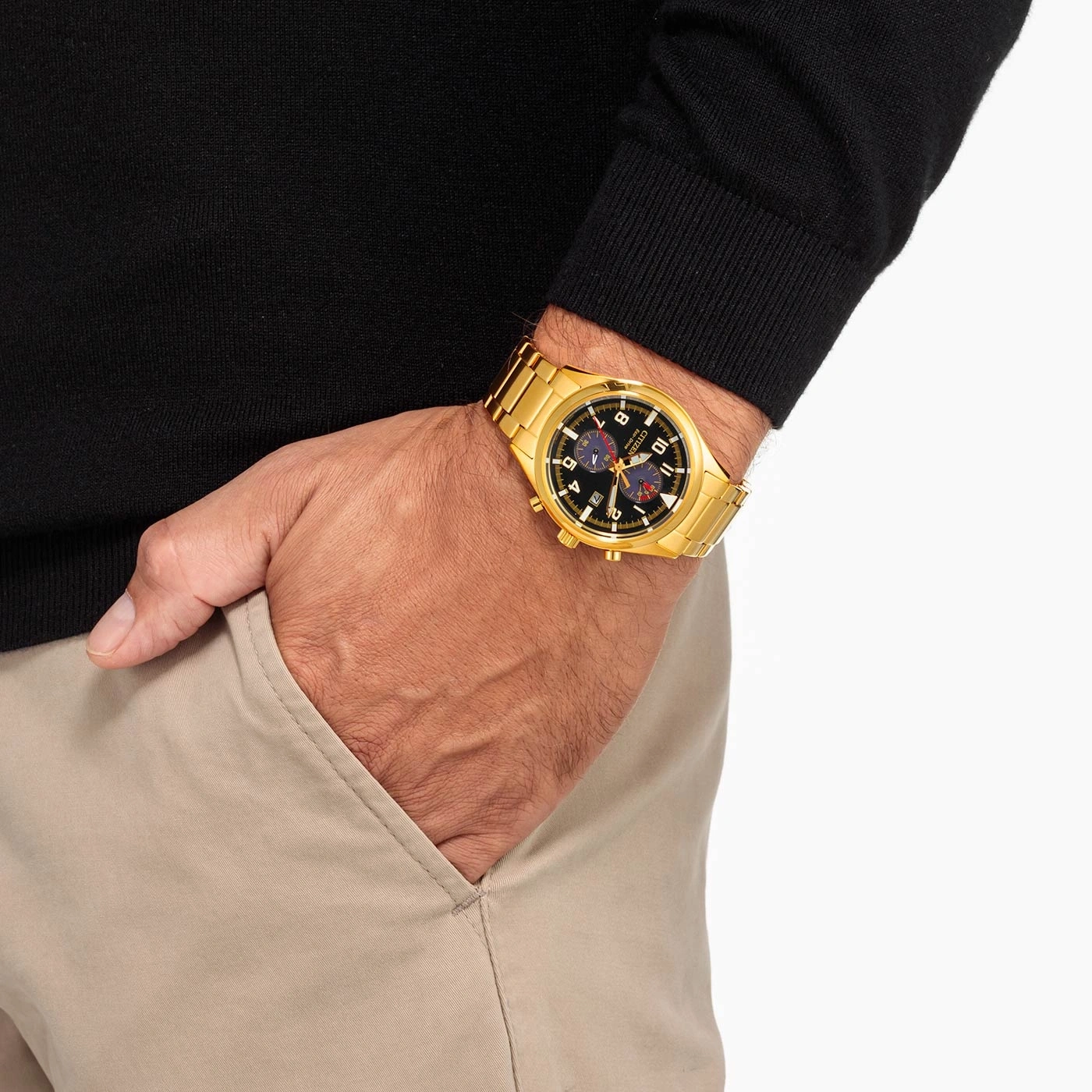 Man met gouden horloge, zwarte trui en beige broek.