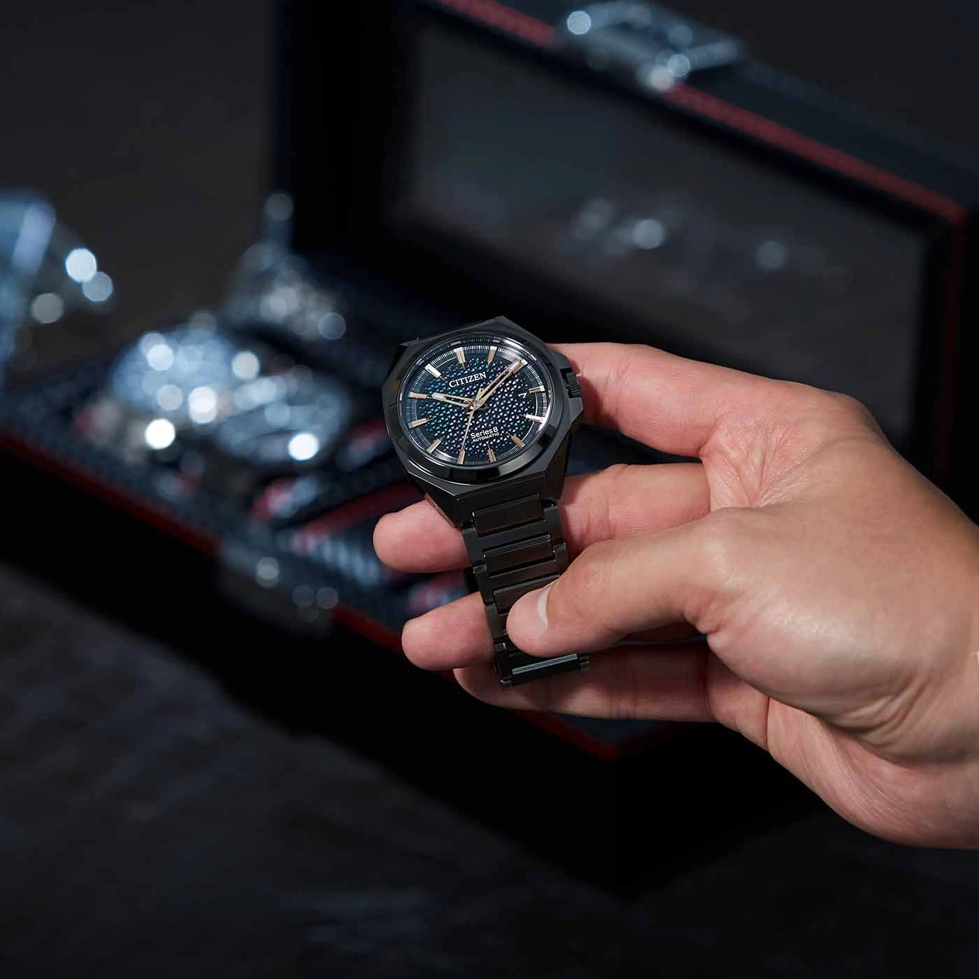 Een persoon die een zwart Citizen-horloge vasthoudt met een donkere achtergrond.