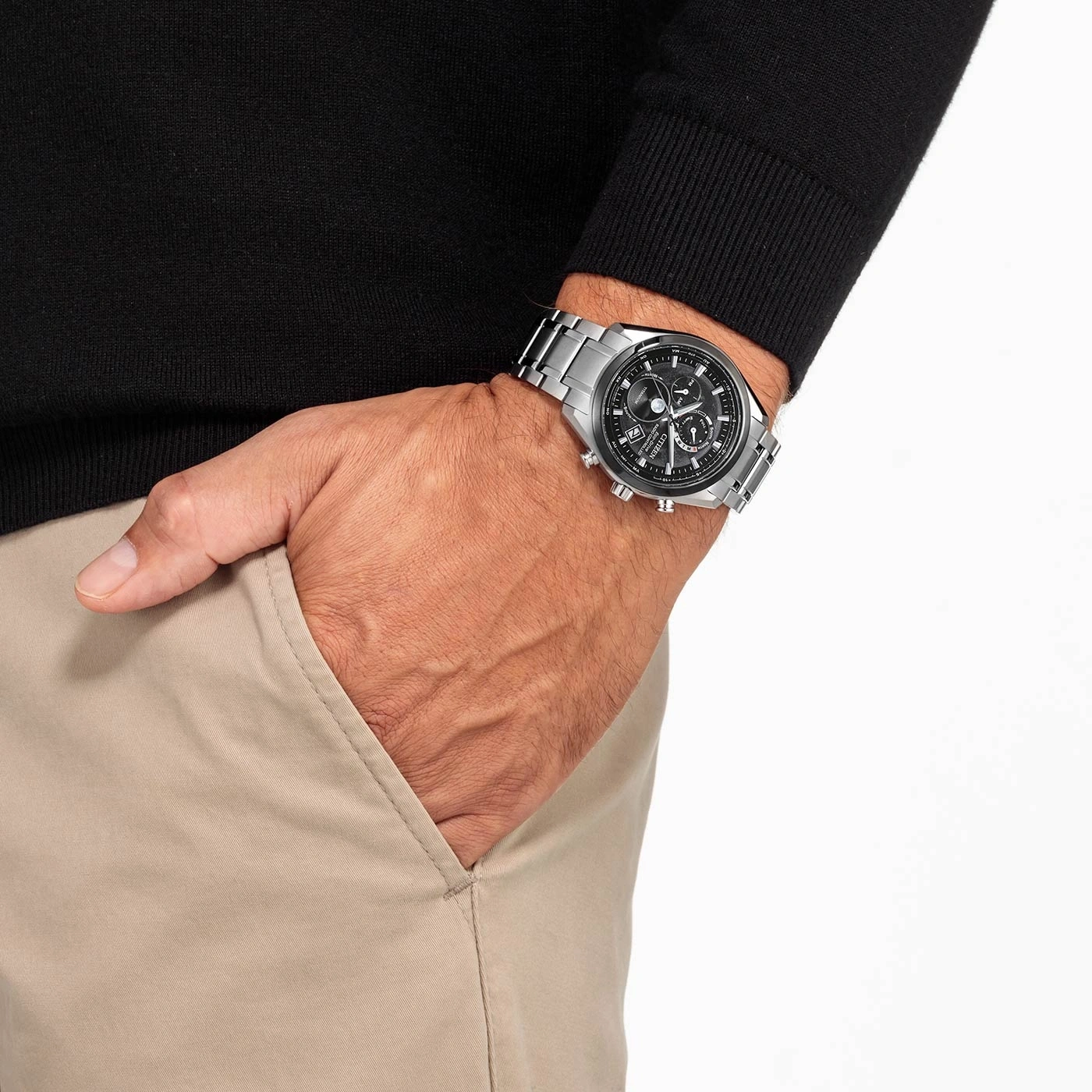Man met horloge, hand in zak, zwarte trui, beige broek