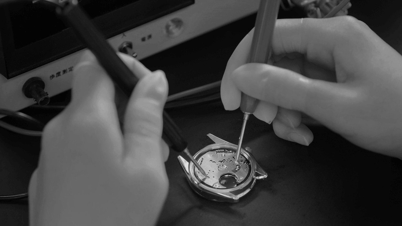 Handen die met gereedschap aan een horloge werken, close-up, zwart-wit.