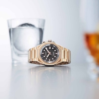 Gouden horloge met zwarte wijzerplaat, glas water en reflecterend oppervlak.