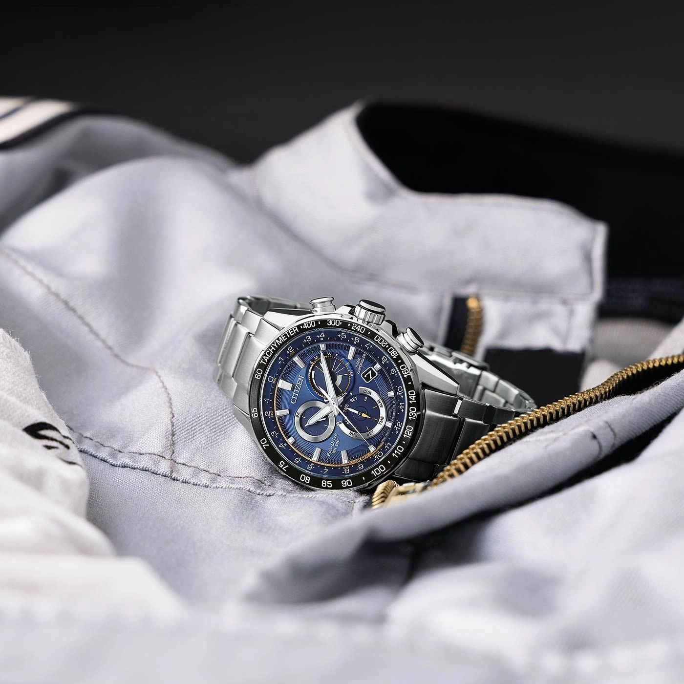 Citizen horloge op een grijze jas met blauwe wijzerplaat en zilveren band.
