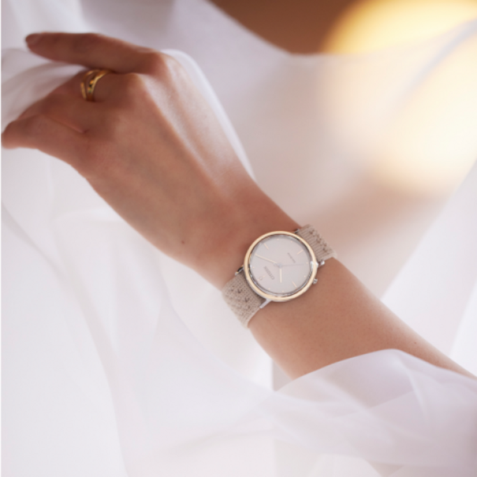 Close-up van een polshorloge met een beige bandje om de pols van een vrouw.