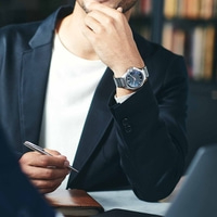 Man in pak met horloge, houdt pen vast, denkt na, zakelijke bijeenkomst, kantoor