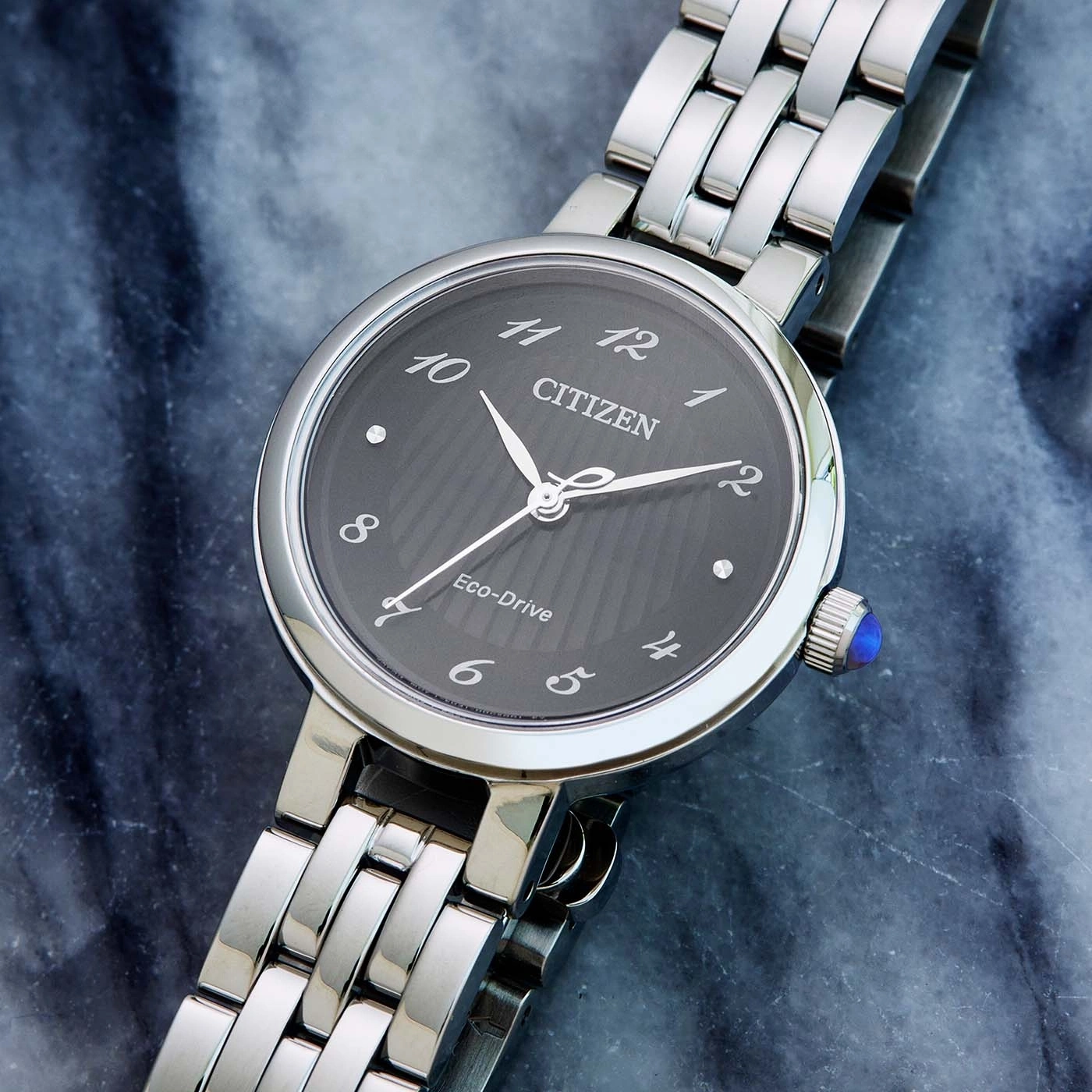 Citizen horloge met donkere wijzerplaat en zilveren band op marmeren oppervlak.