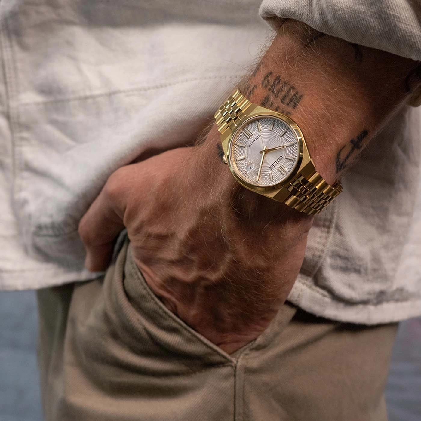 Gouden horloge om de pols van een man met tatoeages.
