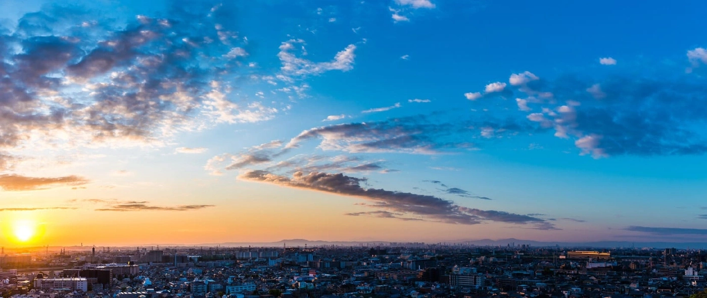 Stadsgezicht bij zonsondergang met een levendige lucht en verspreide wolken boven gebouwen.
