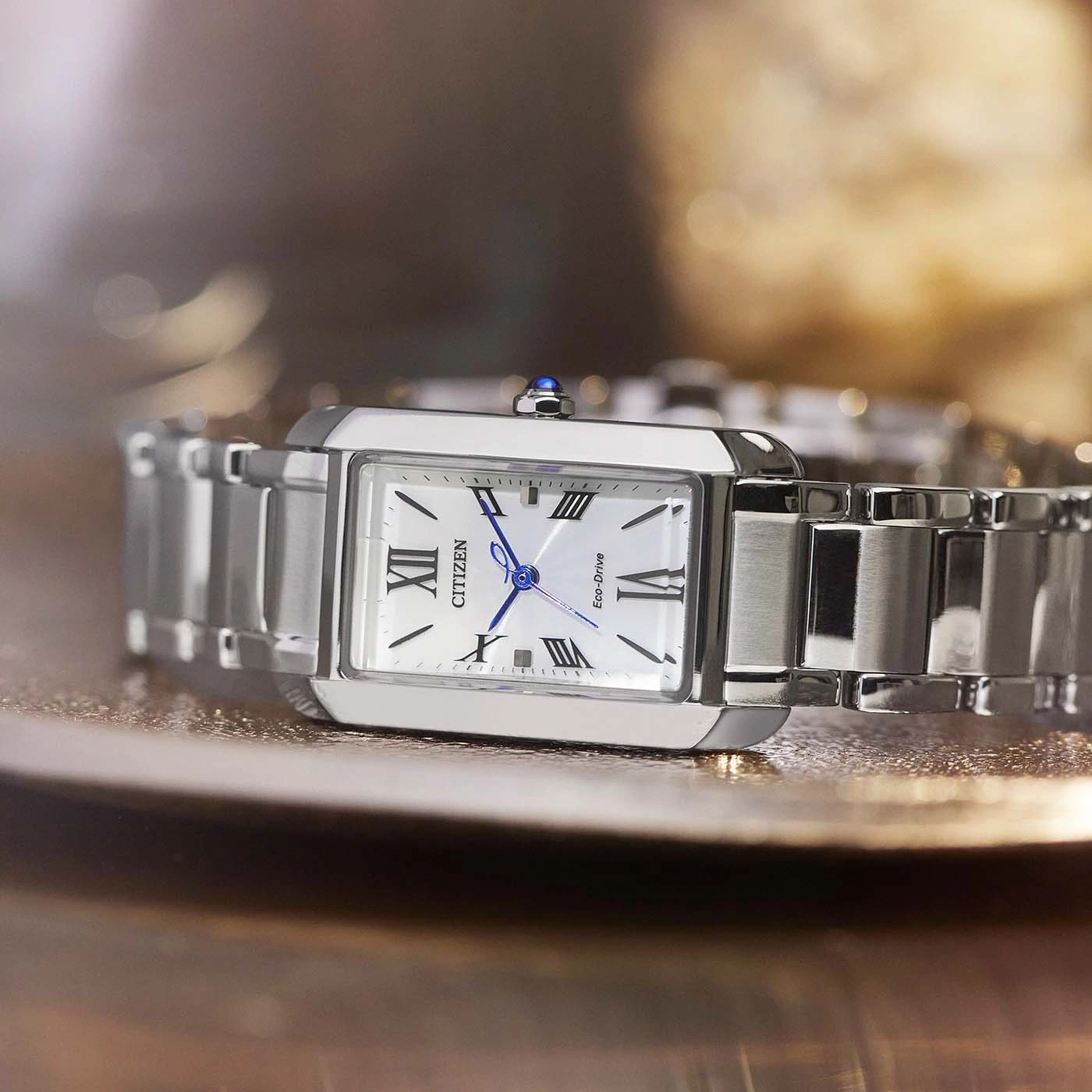 Citizen horloge met witte wijzerplaat en zilveren band op reflecterend oppervlak