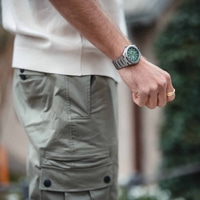 Man met horloge en ring, met groene wijzerplaat en kaki broek.