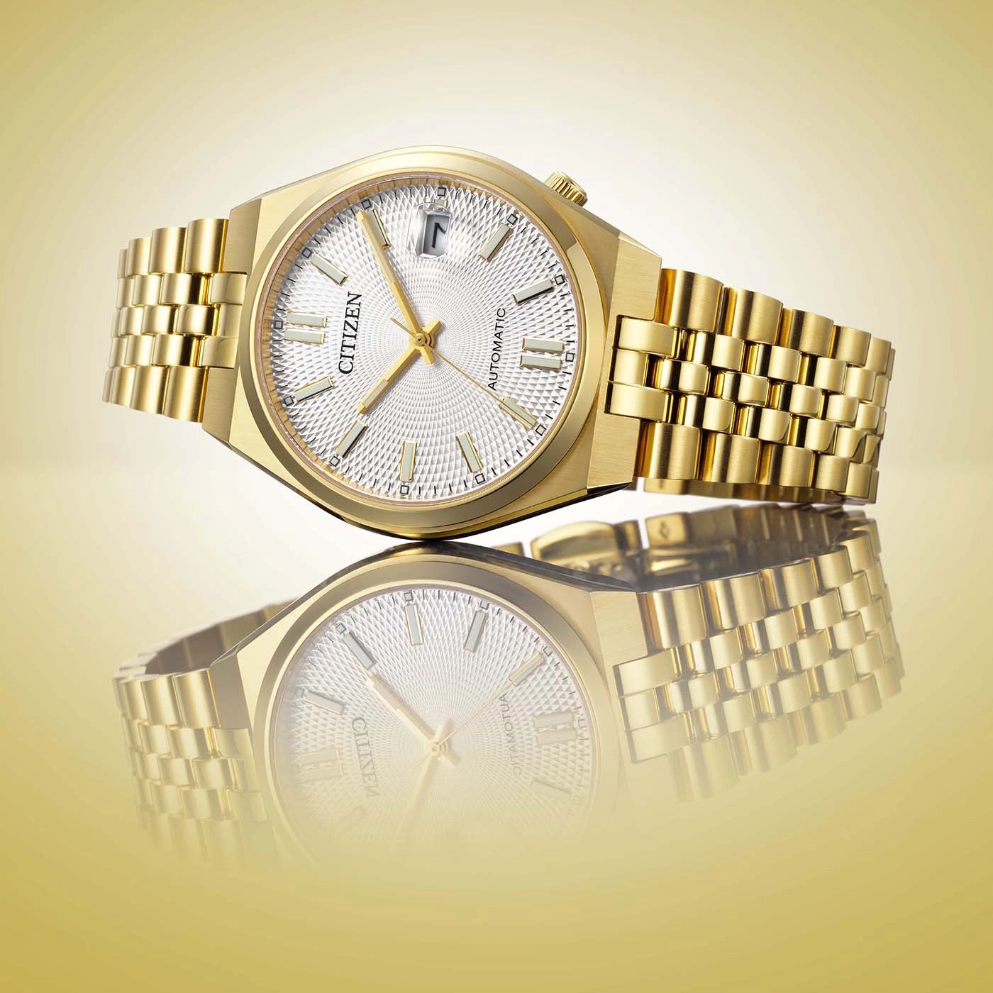 Een close-up studiofoto van een luxe gouden Citizen automatische horloge met witte wijzerplaat en bijpassende band, gereflecteerd op een gouden ondergrond.