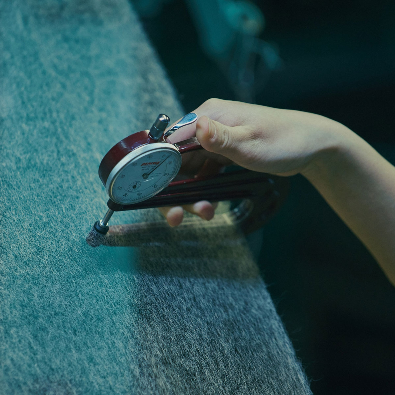 Hand misst mit Messuhr die Dicke eines Stoffes, Nahaufnahme, Detailaufnahme.