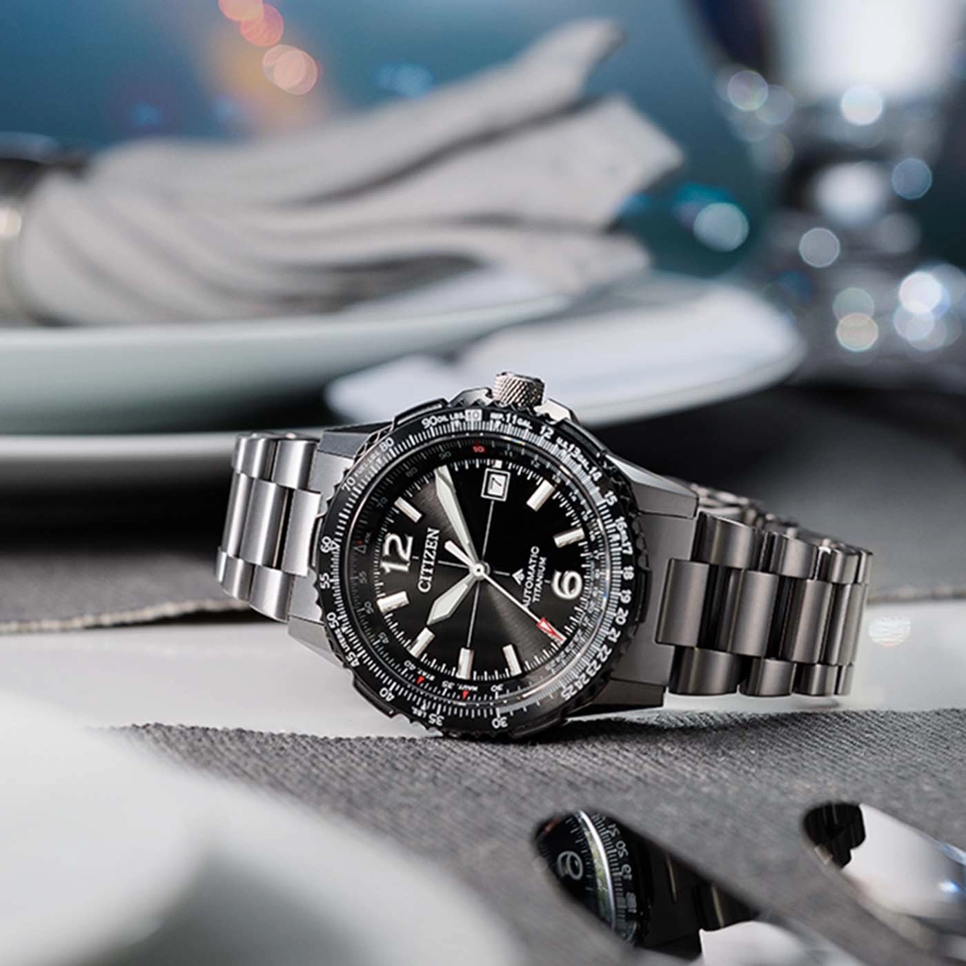 Een zwart Citizen automatisch titanium horloge op een tafel met bestek.