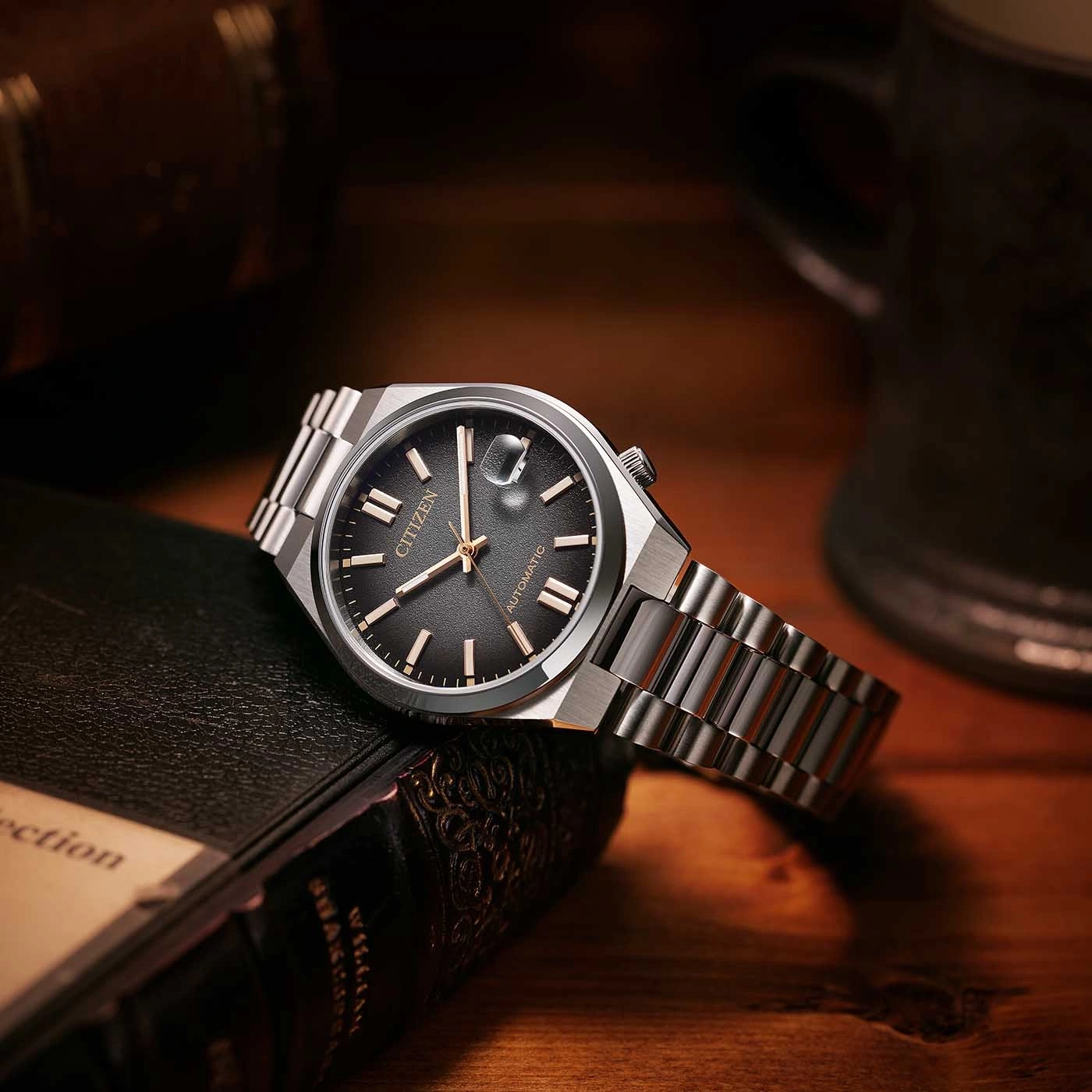 Citizen horloge op een boek, met een donkergrijze wijzerplaat en zilveren band.