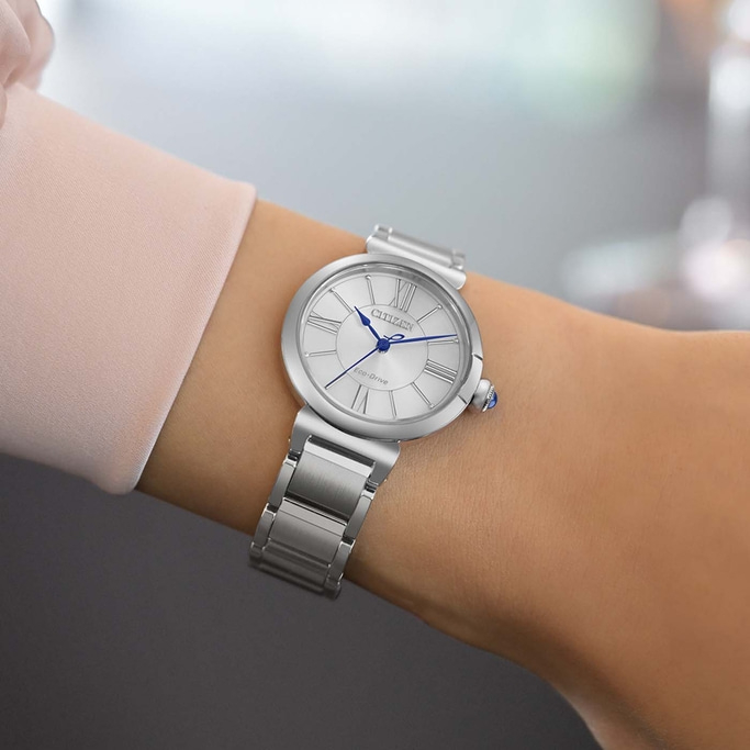 Een vrouw draagt een zilveren Citizen Eco-Drive horloge met Romeinse cijfers.