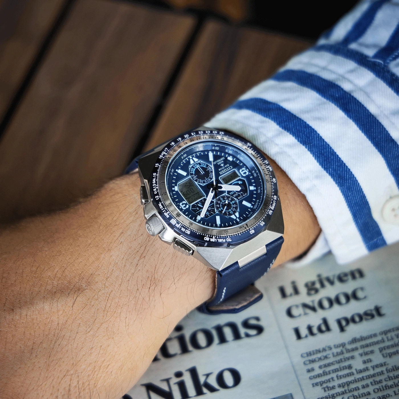 Pols horloge met blauwe band op de arm van een persoon, krant op de achtergrond.