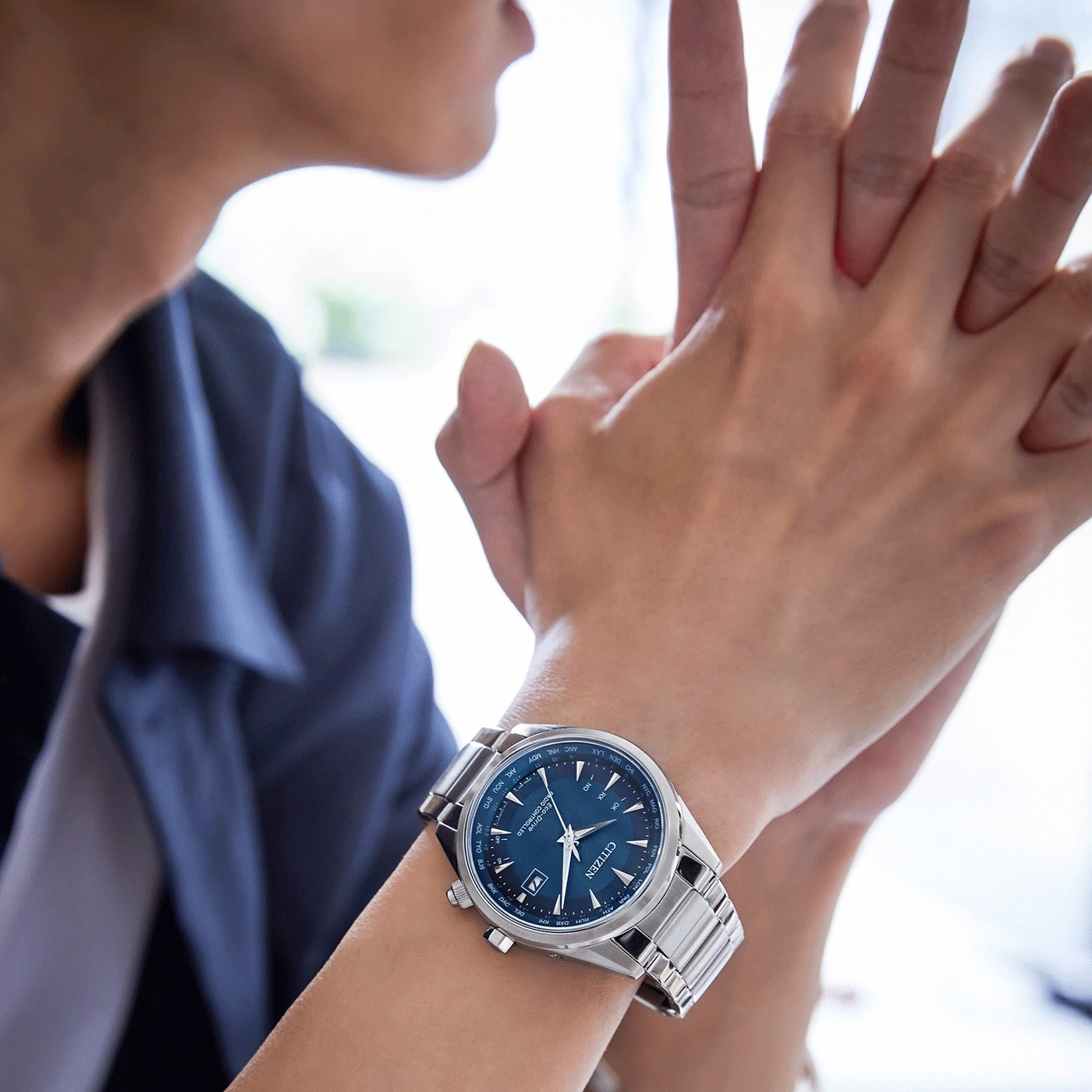 Persoon met een Citizen-horloge met een blauwe wijzerplaat en zilveren band.