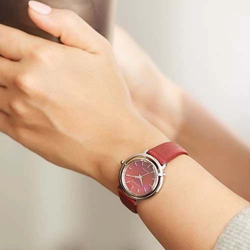 Een pols van een vrouw met een rood horloge. Het horloge heeft een rode band en een zilveren kast.