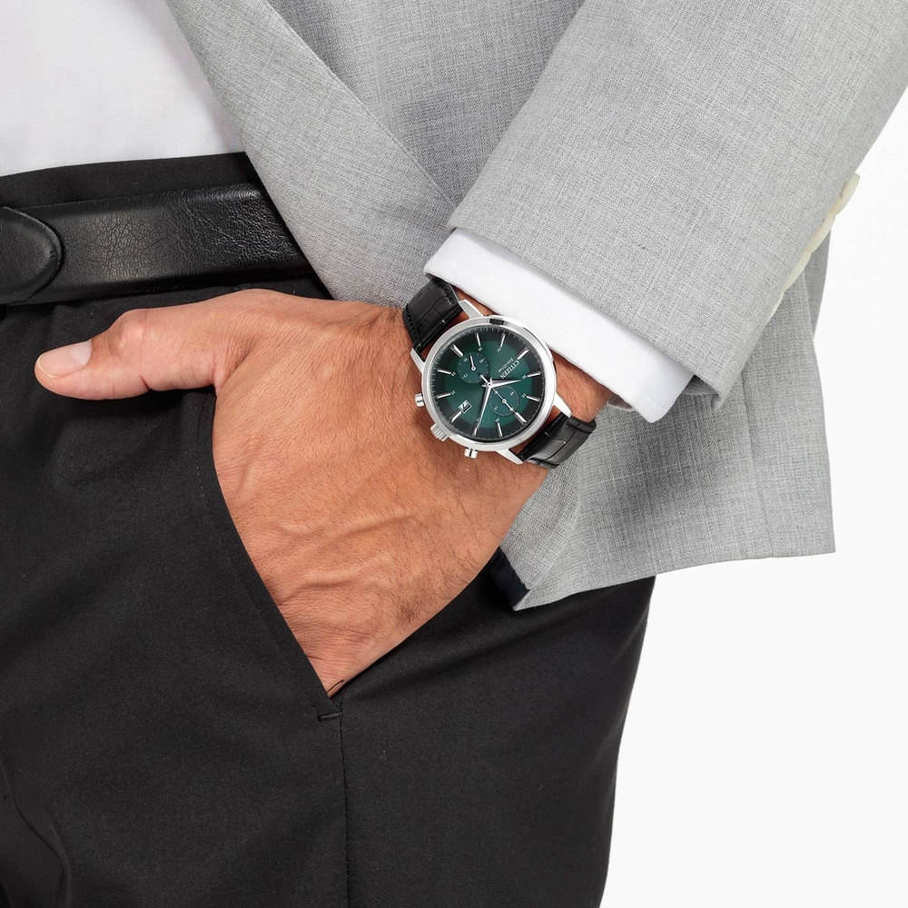 Man met horloge, pak en zwarte broek, hand in de zak.