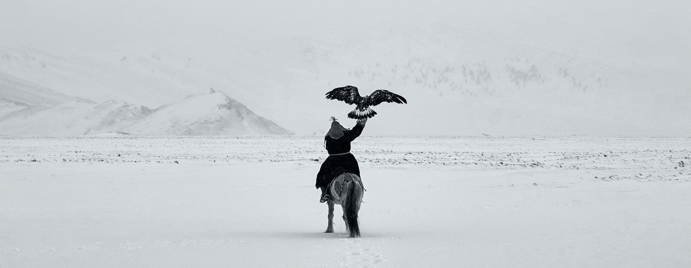 Man te paard met adelaar in besneeuwd landschap, zwart-wit foto