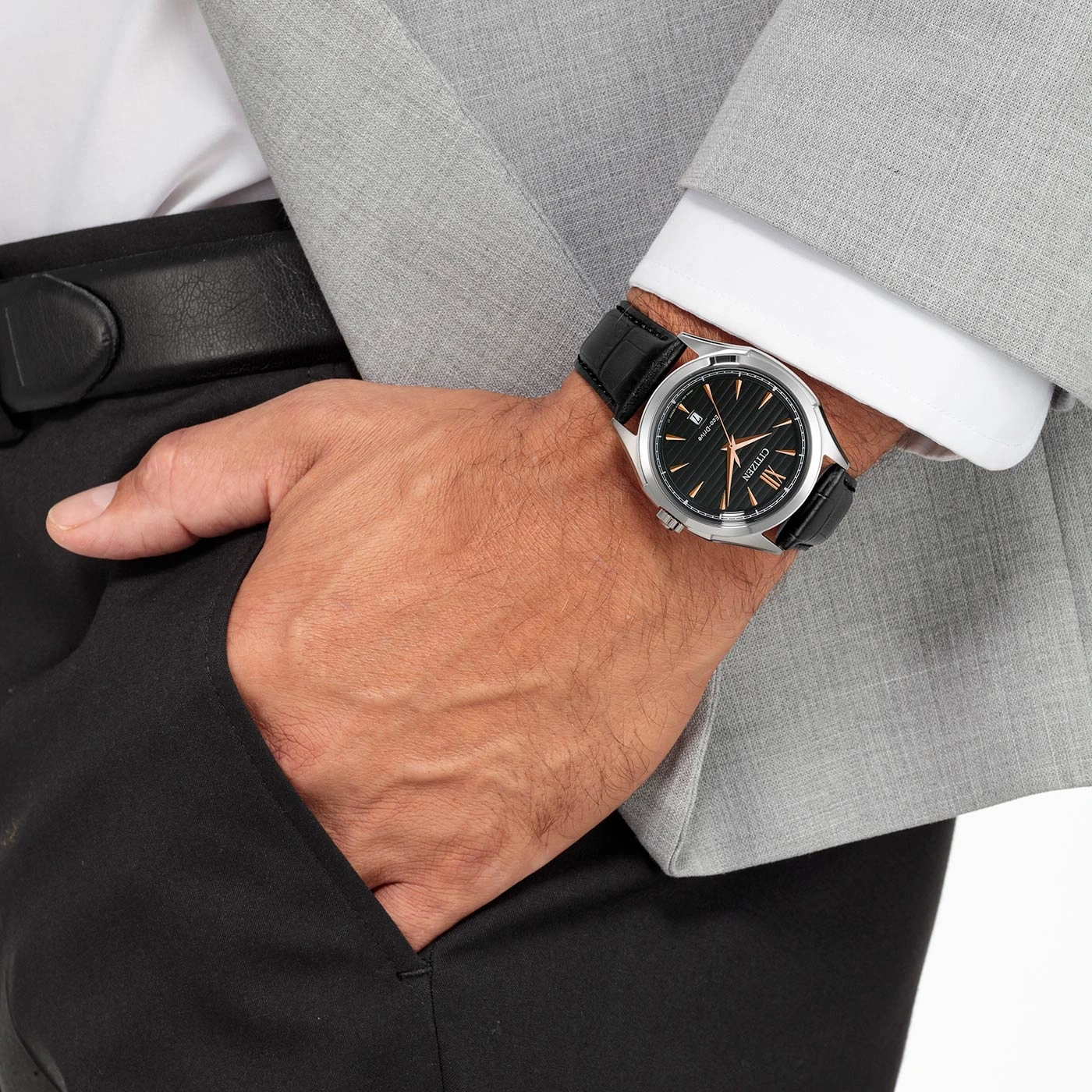 Man met horloge, pak en zwarte broek, hand in de zak.