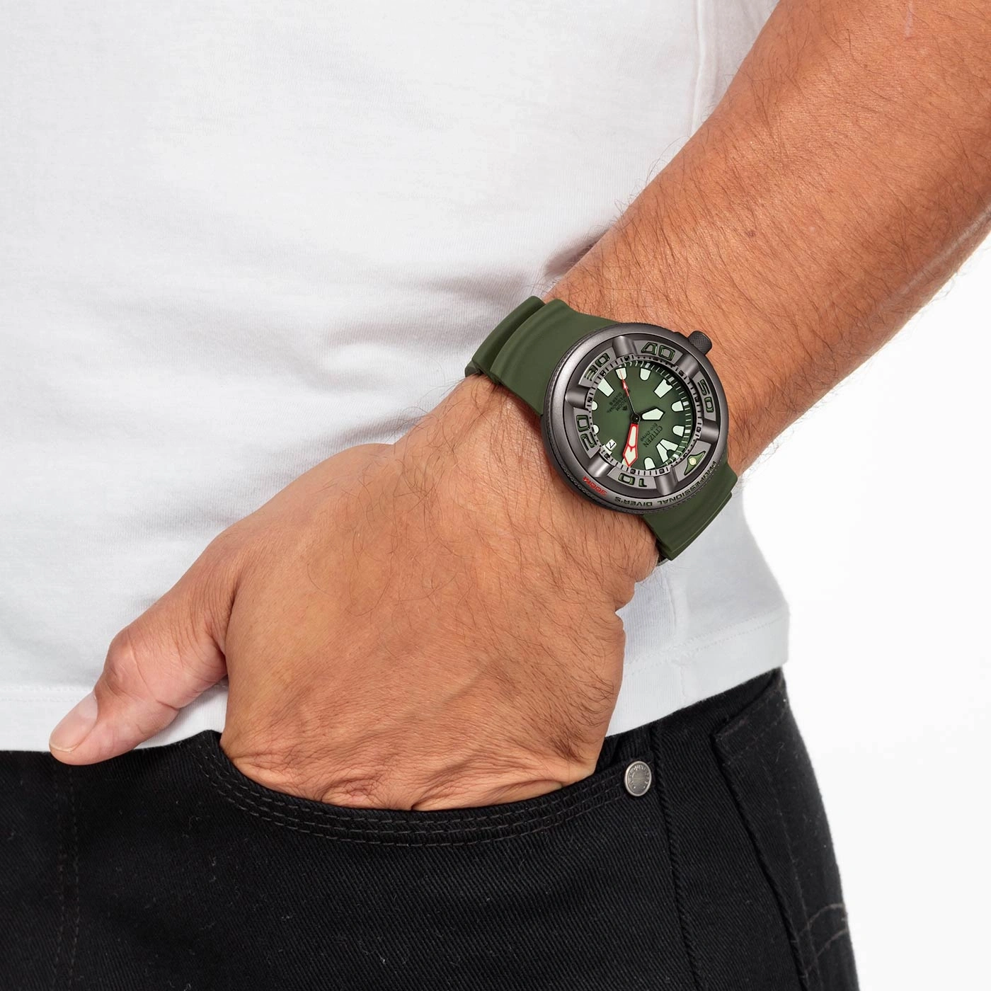 Man met groen horloge, hand in zak, wit shirt, zwarte broek.