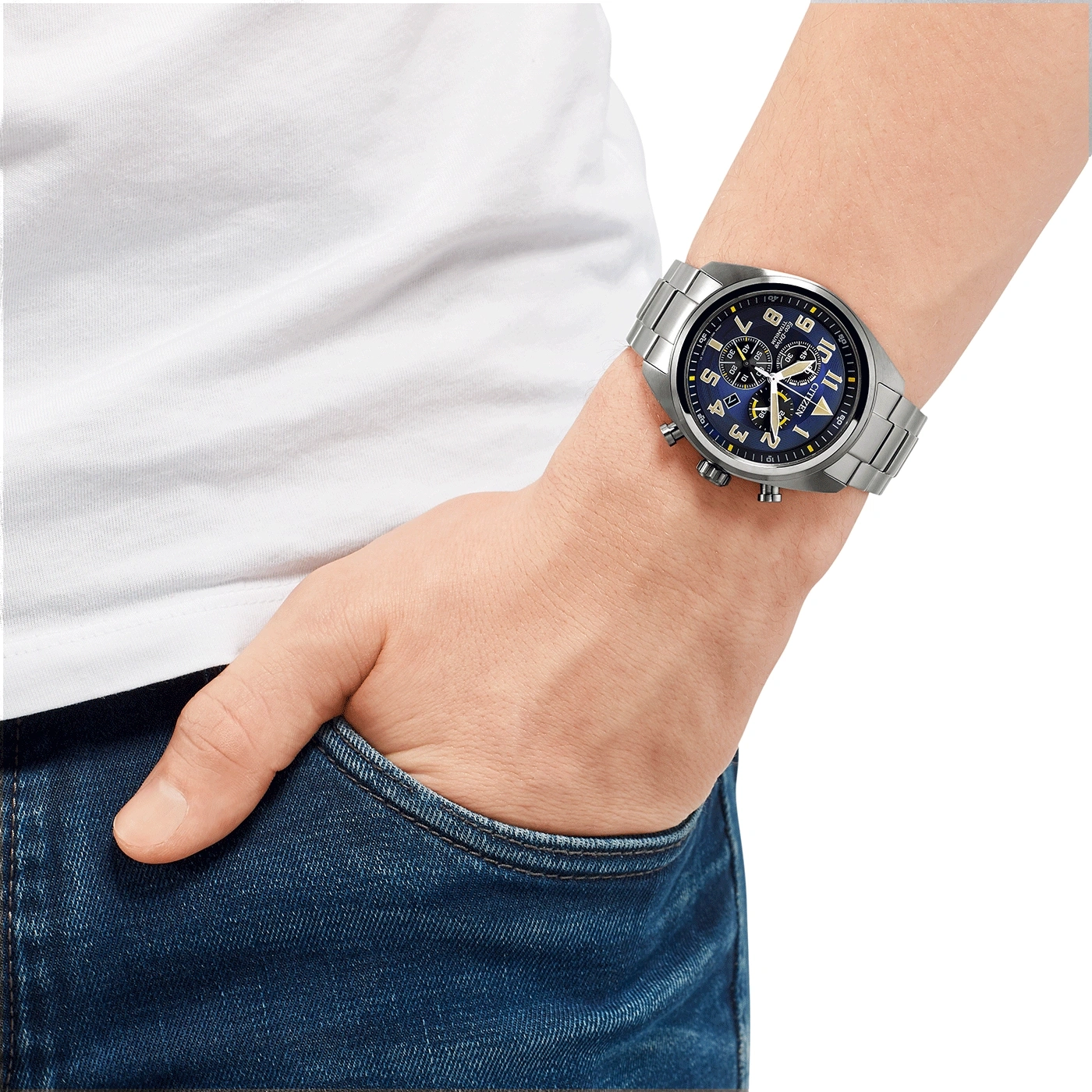 Man draagt zilveren horloge met blauwe wijzerplaat, hand in zak.