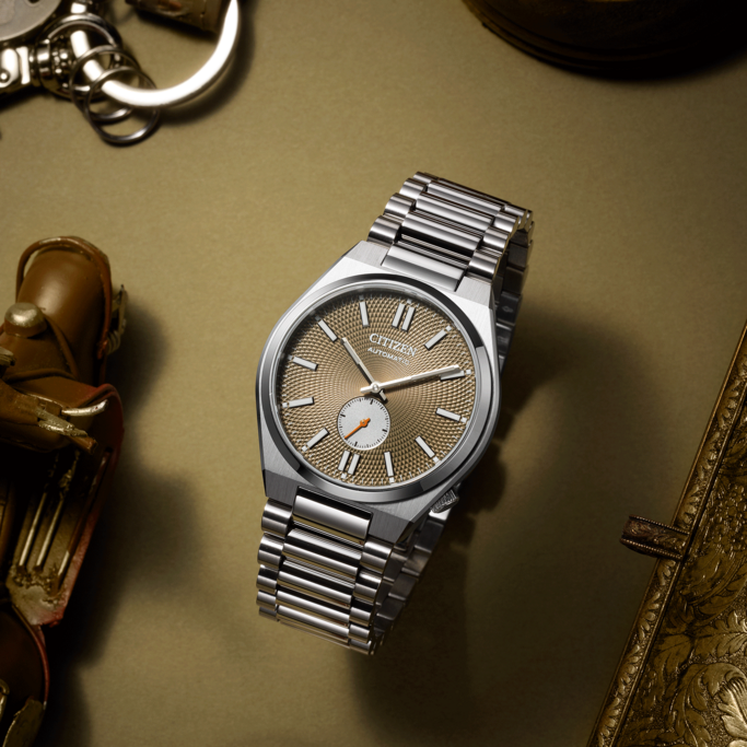 Citizen horloge met zilveren band op gouden oppervlak met accessoires.