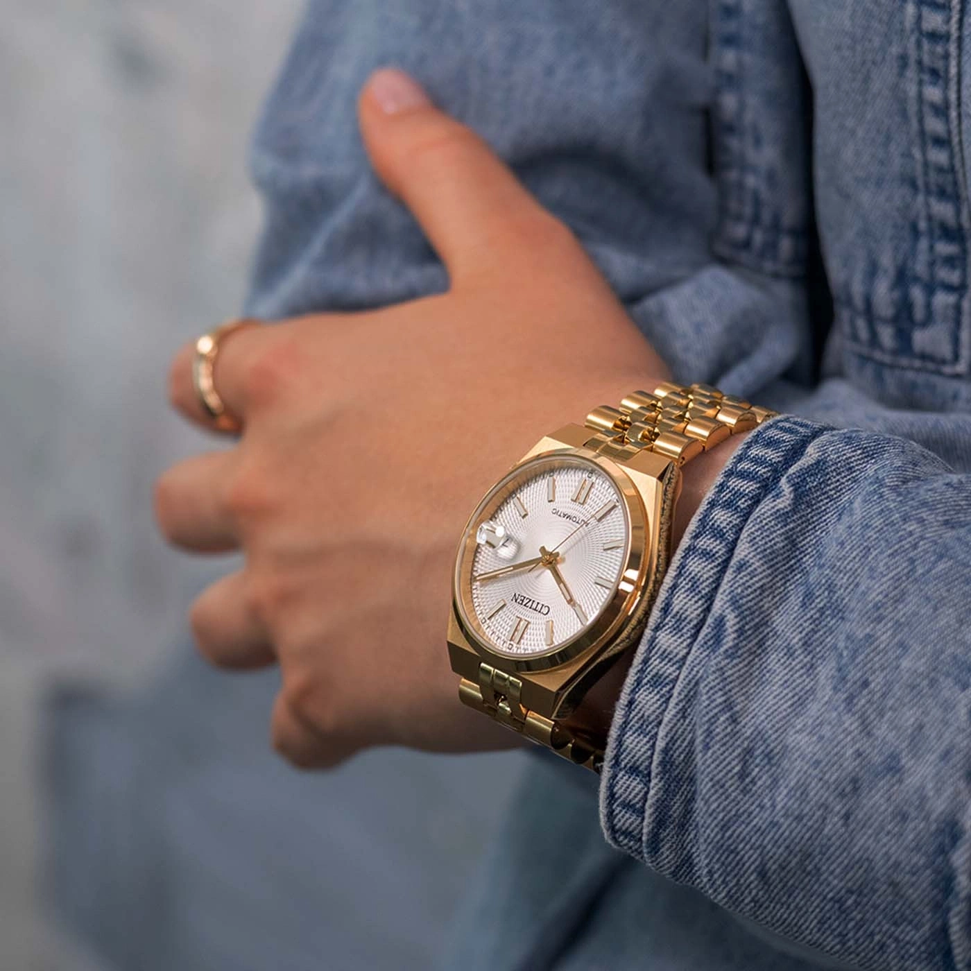 Gouden Citizen horloge om een pols in een spijkerjasje.