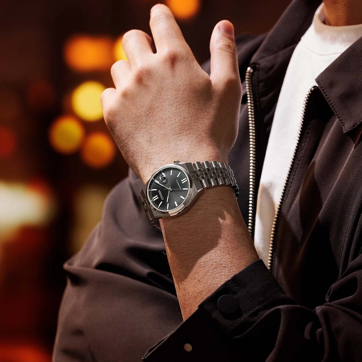 Man draagt zilveren horloge met zwarte wijzerplaat en bruine jas.