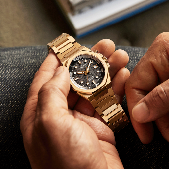 Close-up van een gouden Citizen horloge in de handen van een persoon.