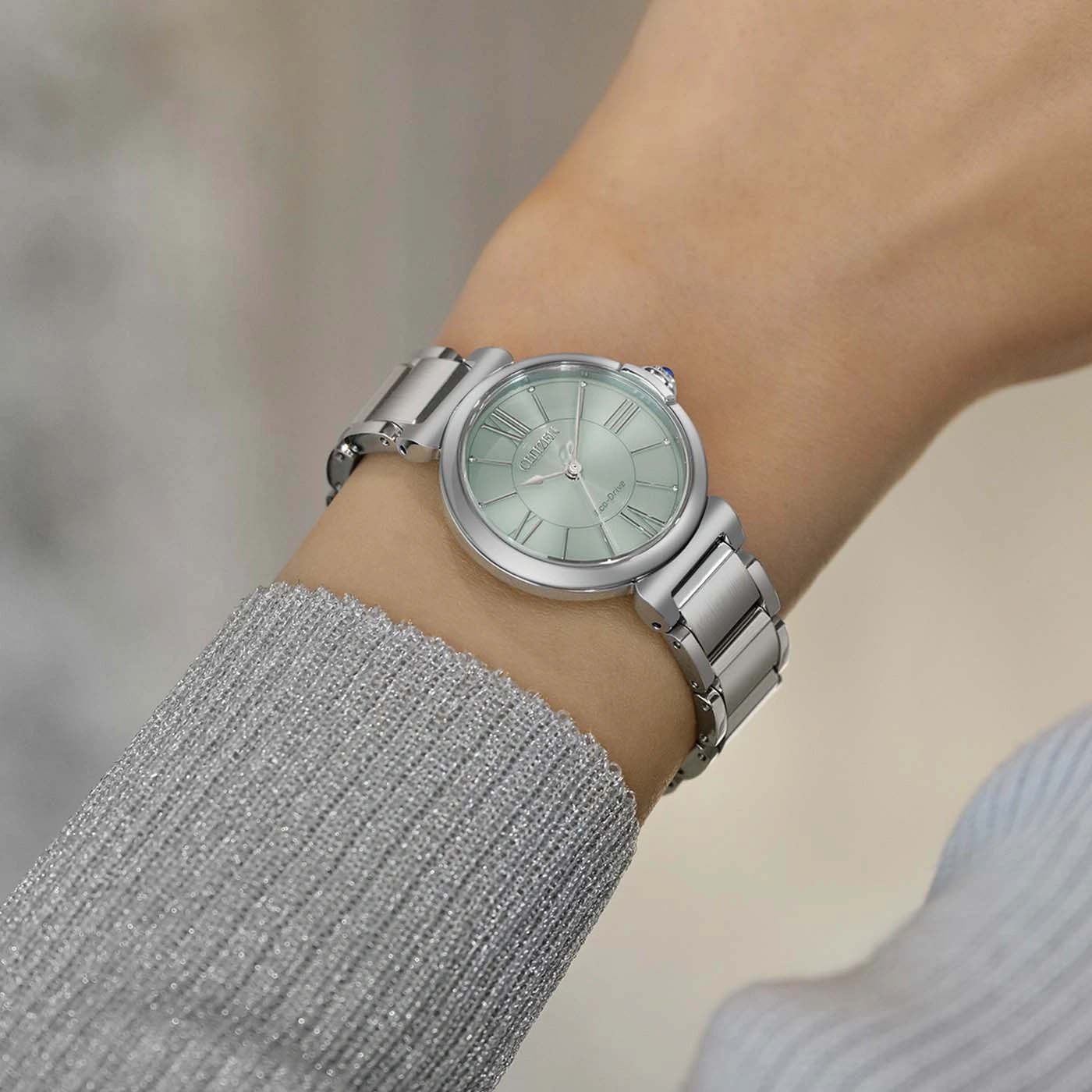 De pols van een vrouw met een zilveren horloge met een lichtgroene wijzerplaat.